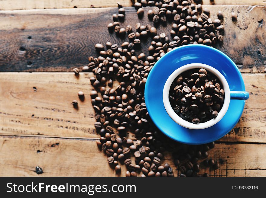 Overhead of coffee beans in blue cup and saucer on rustic wooden boards.