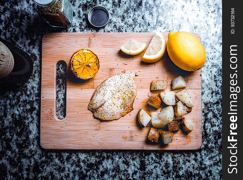 Flat lay of fillet of fish on cutting board with lemons and roasted potatoes on granite kitchen counter with spices. Flat lay of fillet of fish on cutting board with lemons and roasted potatoes on granite kitchen counter with spices.