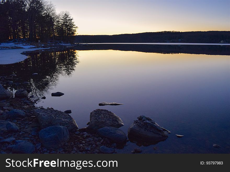 Lights of sunset reflecting in calm waters from rocky shores.