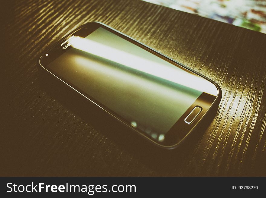 A close up of a modern smartphone on a wood surface.