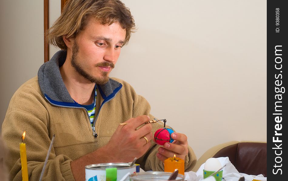 Man painting Easter egg with technique of wax putting