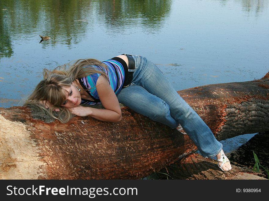 Beautiful female model laying on fallen tree on the lake. Beautiful female model laying on fallen tree on the lake