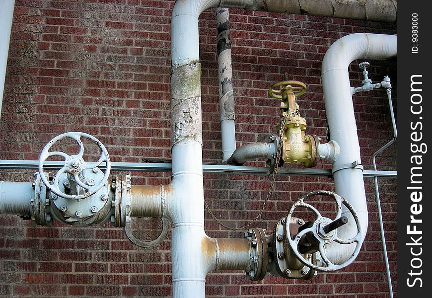 Old blue valves and piping in an abandoned chemical plant against a red brick wall. Old blue valves and piping in an abandoned chemical plant against a red brick wall.