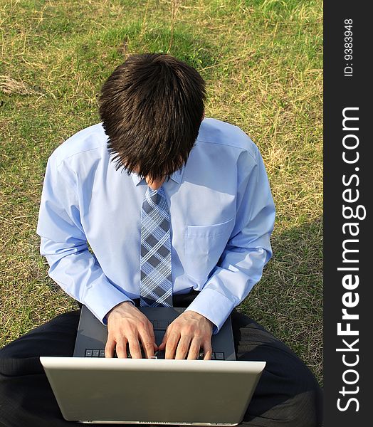 Businessman sitting on the grass with laptop, very concentrated, working hard