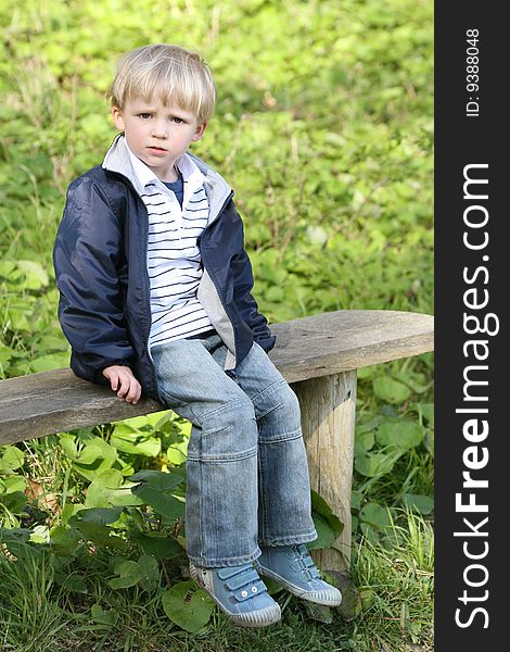 This small boy is sitting on the bench and he is not really happy. This small boy is sitting on the bench and he is not really happy