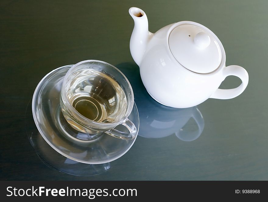 White tea in transparent cup and white teapot on the table