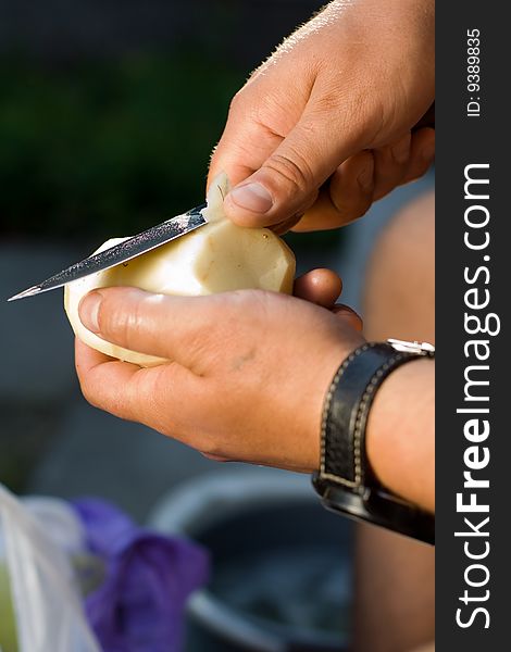 Men's hands with a knife clean potatoes.