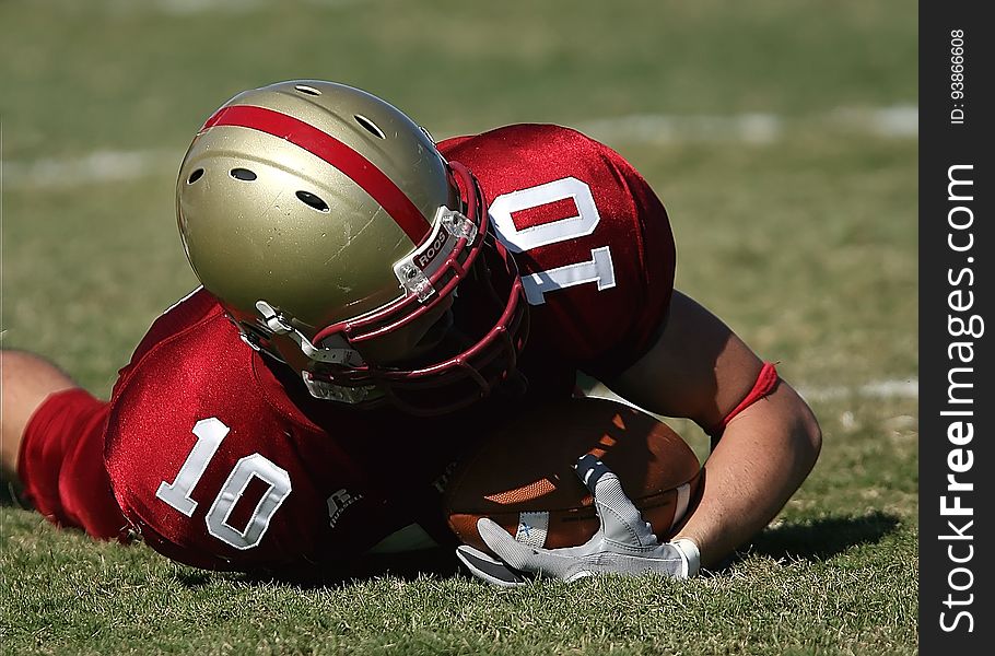 Man in Red White Football Jersey and Grey Red Helmet Holding Football and Lying on Green Grass Field
