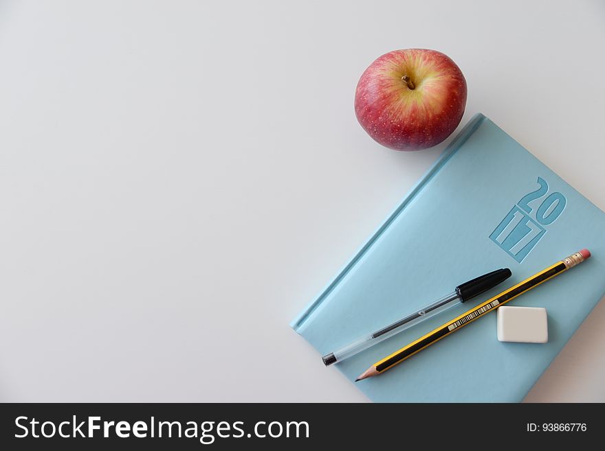 A yearly planner with pens next to an apple.