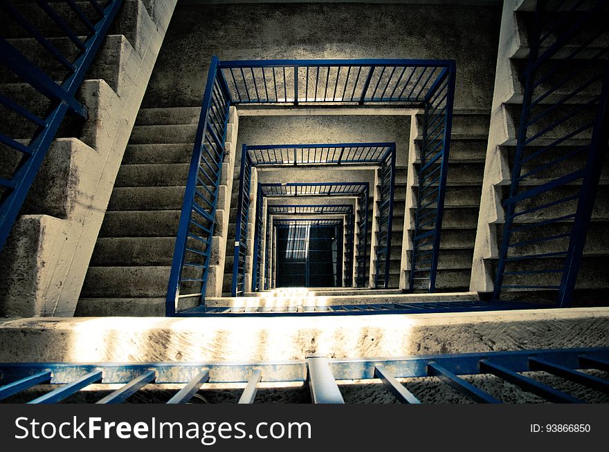 View down a concrete staircase covering many floors with safety railings for a building under construction. View down a concrete staircase covering many floors with safety railings for a building under construction.