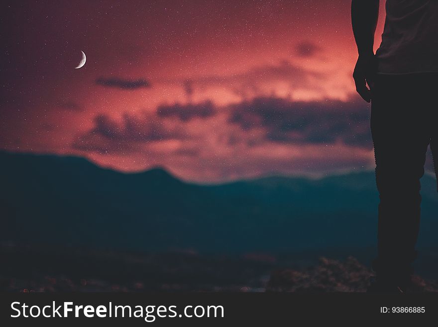 A silhouette of a person watching a crimson sky as night falls.