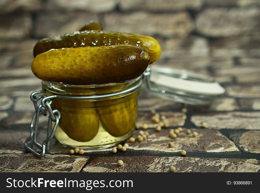 A closeup of pickles in a jar on a cobblestone street.