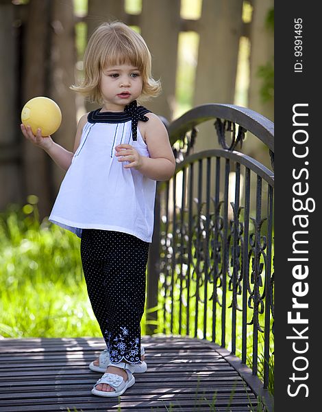 Little girl standing on bridge with yellow ball in her hand. Little girl standing on bridge with yellow ball in her hand