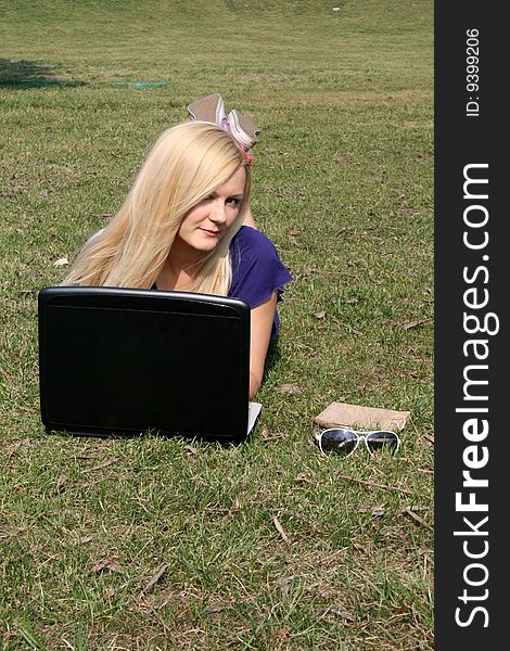 Smiling girl with a laptop lying on grass