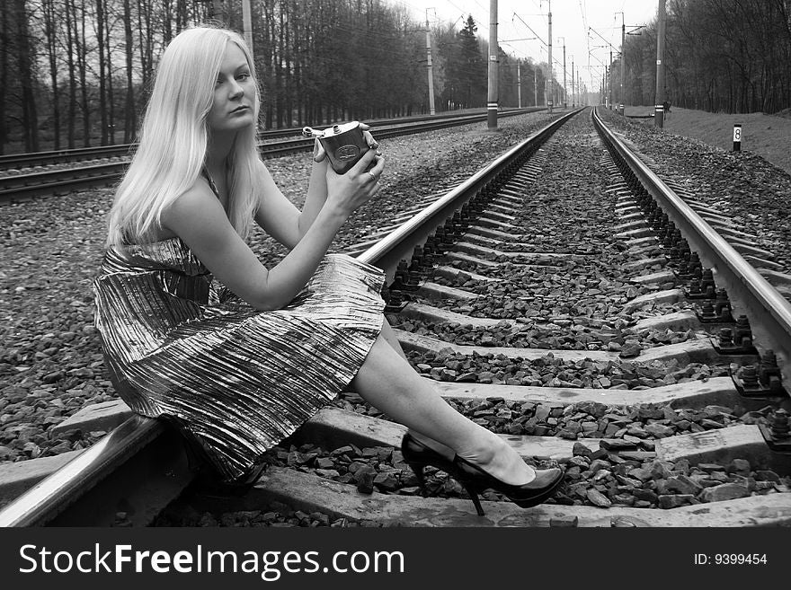 Pretty girl with a flask sitting near railroad