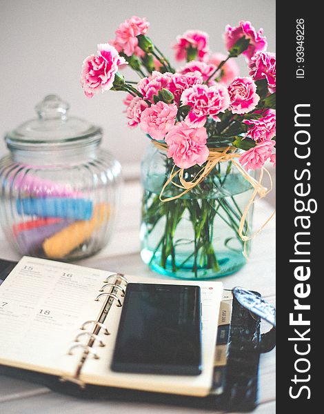 A journal with a mobile phone on a table with a bouquet of carnations. A journal with a mobile phone on a table with a bouquet of carnations.