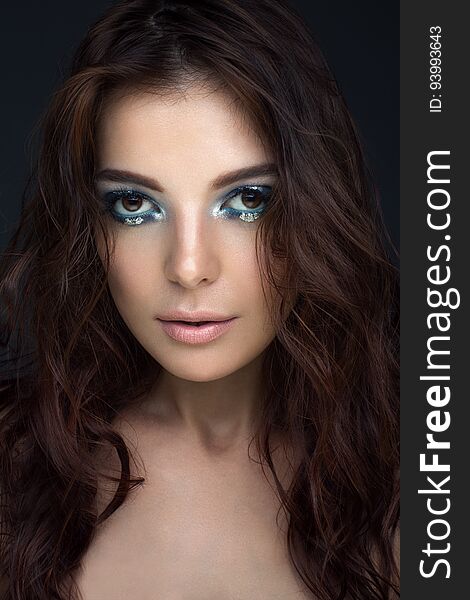 Close-up portrait of girl with dark hair with blue eyeshadow and silver dots, looking at the camera. Vertical photo