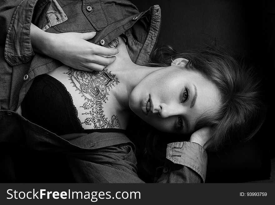 Black and white portrait of a girl in a denim shirt and black bra with a mehendi on her chest lying on the sofa, top view. Horizontal photo