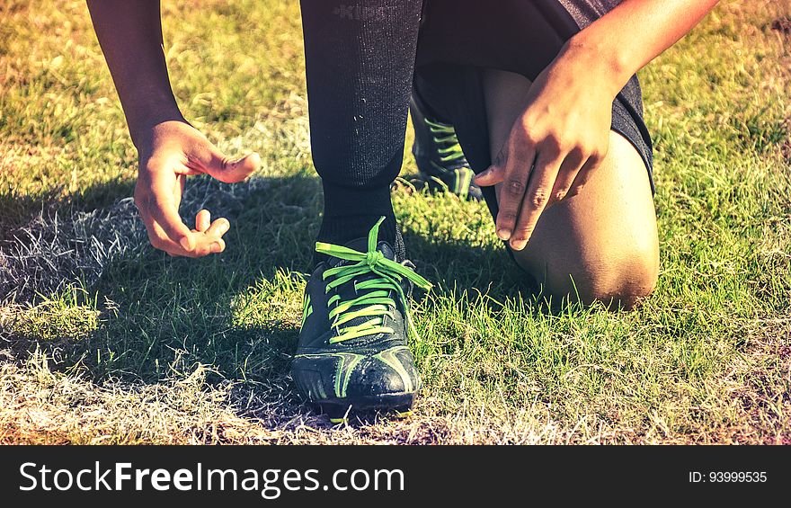 Man kneeling in grassy sports field wearing athletic shoes. Man kneeling in grassy sports field wearing athletic shoes.