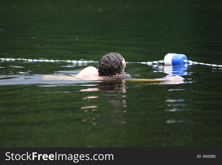 A man swims inside a roped area of a resort lake beach. A man swims inside a roped area of a resort lake beach