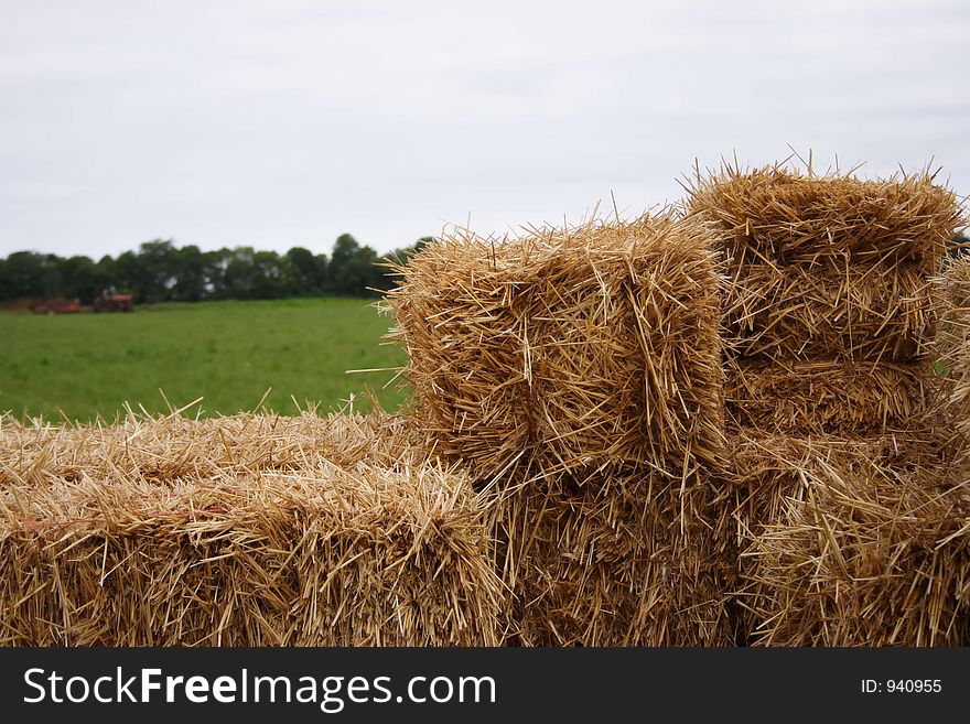 A wagon of straw in the foreground with a farmer working in the background. A wagon of straw in the foreground with a farmer working in the background