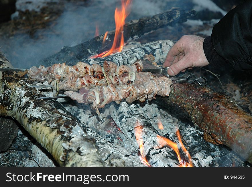 Grilled pork on bonfire and man hand