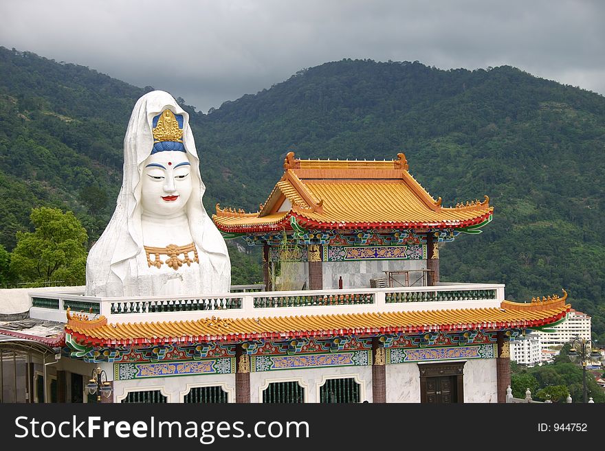Large statue of a Buddha and an elaborate Chinese style temple in front of tree covered mountain. Large statue of a Buddha and an elaborate Chinese style temple in front of tree covered mountain
