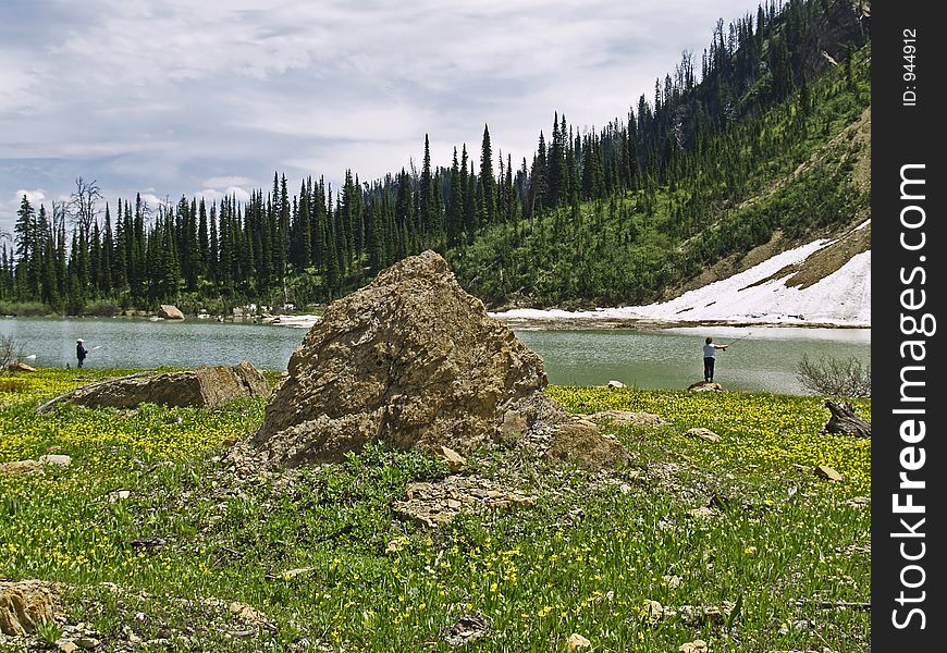 This fishing scene with the two anglers, meadow of glacier lilies, rocks, alpine lake, snowfields and forest was taken in the Great Bear Wilderness of MT. This fishing scene with the two anglers, meadow of glacier lilies, rocks, alpine lake, snowfields and forest was taken in the Great Bear Wilderness of MT.