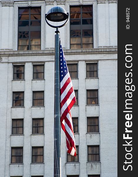 The flag of the United States hangs from a pole with an older building as the background. The flag of the United States hangs from a pole with an older building as the background