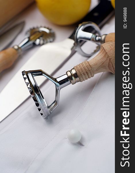 An assembly of chef's tools of trade sitting on a new chef's uniform. a couple of lemons in the background. An assembly of chef's tools of trade sitting on a new chef's uniform. a couple of lemons in the background.