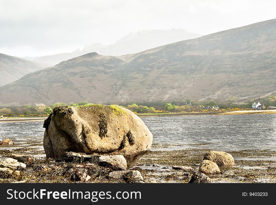 Rock on Lochranza with mountains in the haze. Rock on Lochranza with mountains in the haze