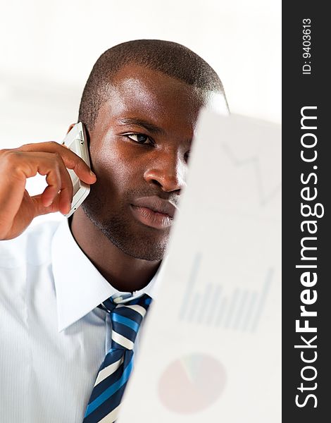 Young adult afro-american businessman examining charts and talking on the phone. Young adult afro-american businessman examining charts and talking on the phone