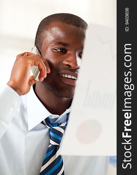 Young adult afro-american businessman examining charts and talking on the phone. Young adult afro-american businessman examining charts and talking on the phone