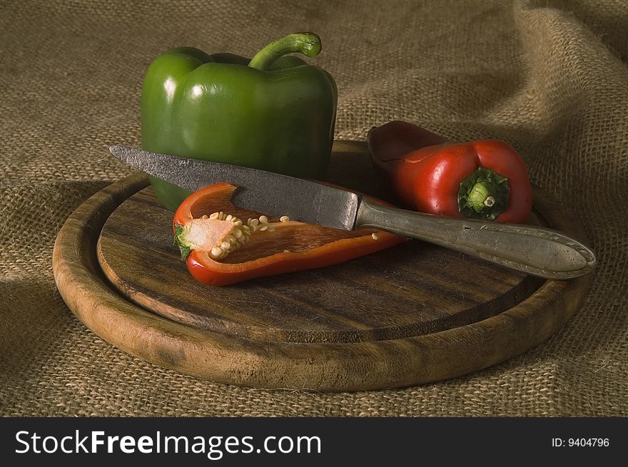 Paprikas with knife on wooden plate