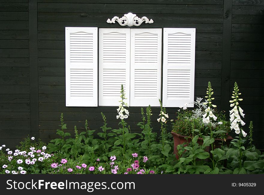 An simple yet ornate white window sit on the outside of a home above a flower garden. An simple yet ornate white window sit on the outside of a home above a flower garden.