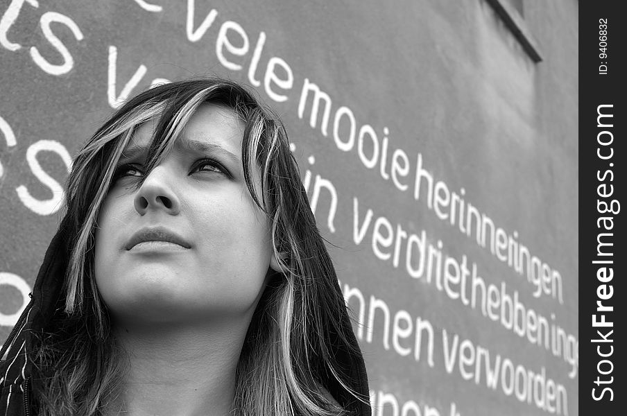 Girl standing in front of a wall with writings on it.
The words on the background means in Dutch: many beautiful memories, to have sorrow, find words.