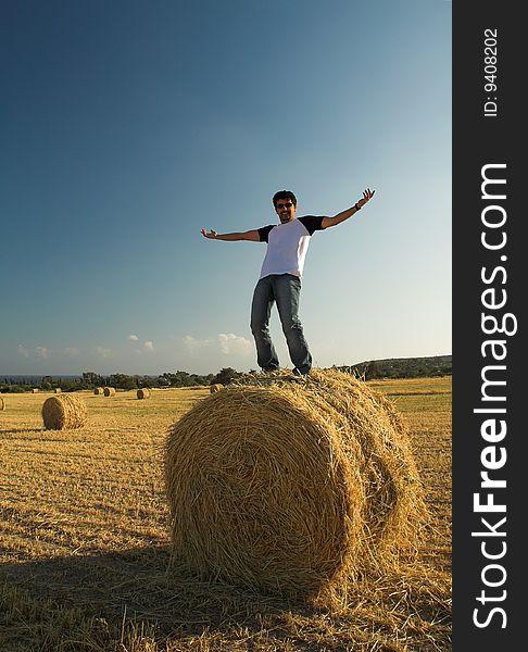 Young man standing on a haystack with arms open wide. Young man standing on a haystack with arms open wide