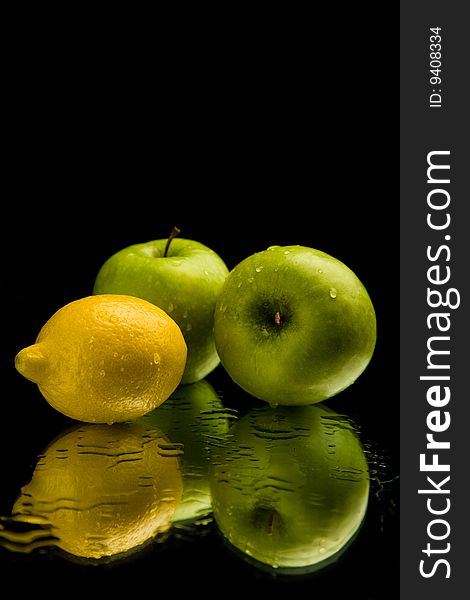 Apple and lemon on mirror over black