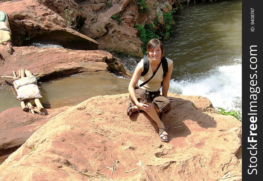 A  woman is sitting on a rock by a waterfall. A  woman is sitting on a rock by a waterfall