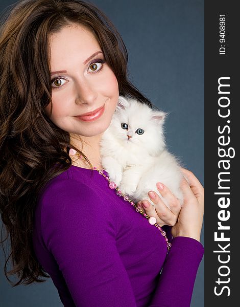 Beautiful girl in purple dress holding little white kitten studio shot