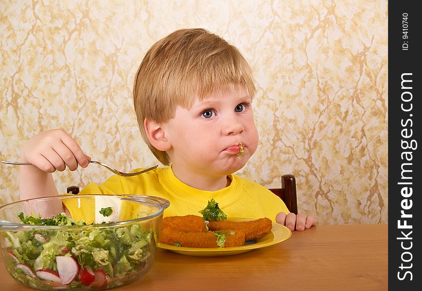 The little boy eats fresh salad. The little boy eats fresh salad