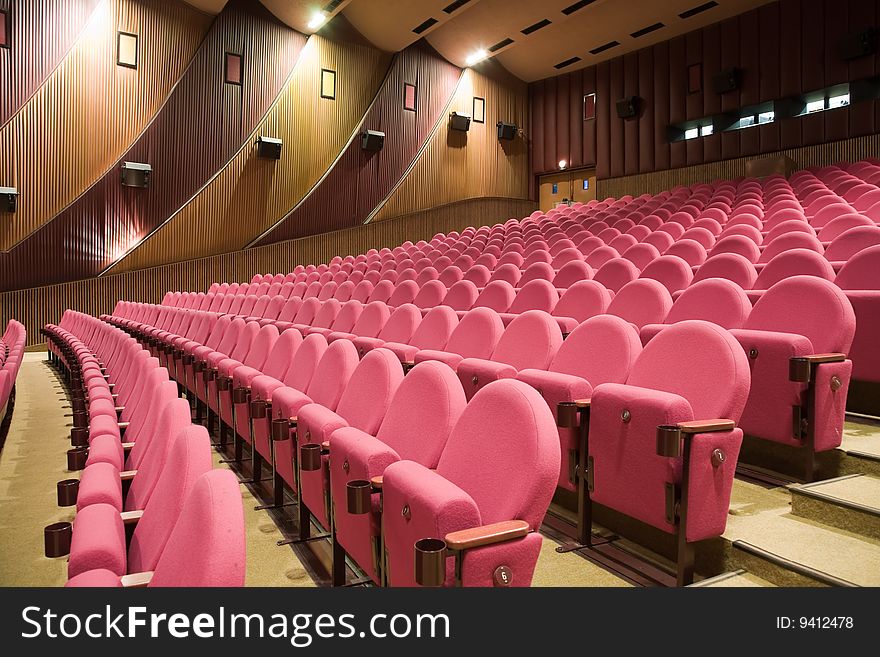 Interior of cinema auditorium with walls and ceiling decoration and line of pink chairs. Interior of cinema auditorium with walls and ceiling decoration and line of pink chairs.