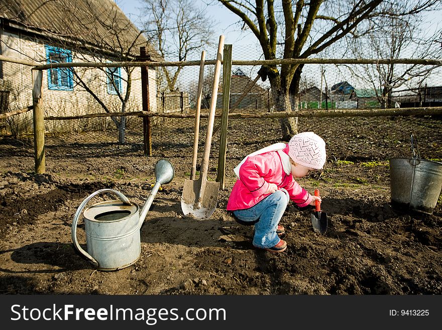 A pretty little girl squatting down on the ground in her grandfather kitchen garden cultivating soil with a toy spade. A pretty little girl squatting down on the ground in her grandfather kitchen garden cultivating soil with a toy spade