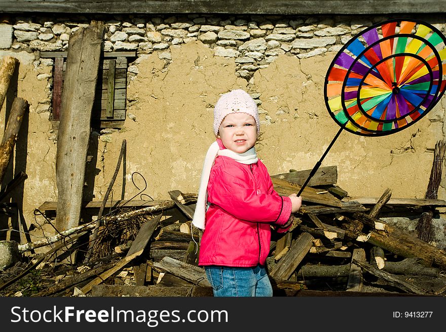 A pretty  little  girl playing  with  her plaything on a background of an old  barn in the countryside. A pretty  little  girl playing  with  her plaything on a background of an old  barn in the countryside