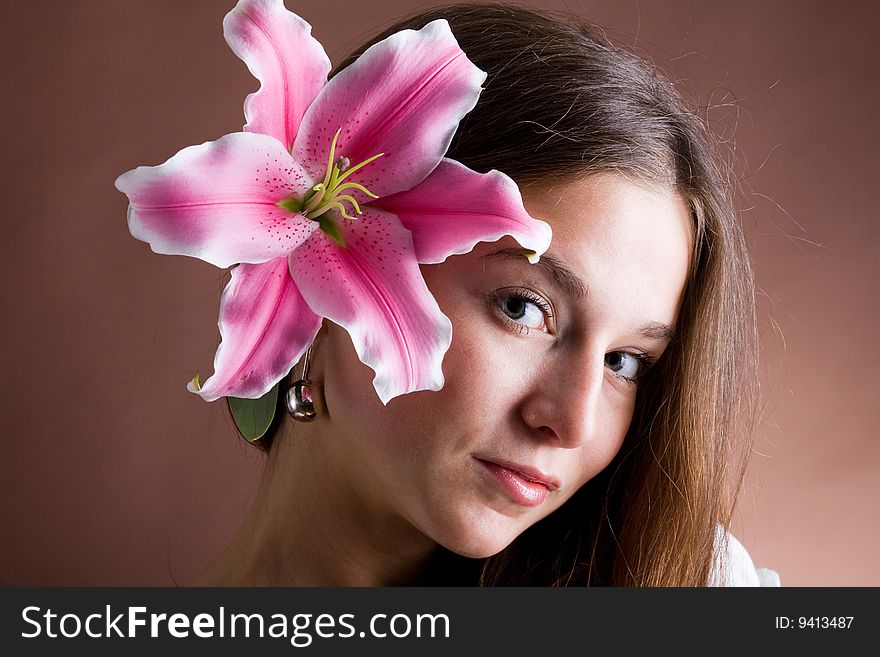A pretty young woman with long brown hair posing with a pink lily near her face. A pretty young woman with long brown hair posing with a pink lily near her face
