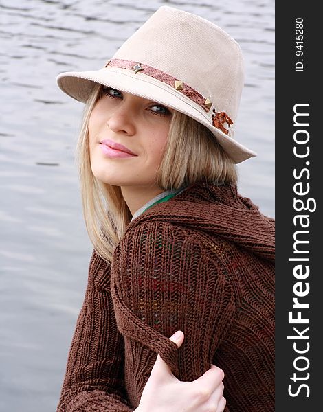 Blonde In Hat Sits On Coast Lake