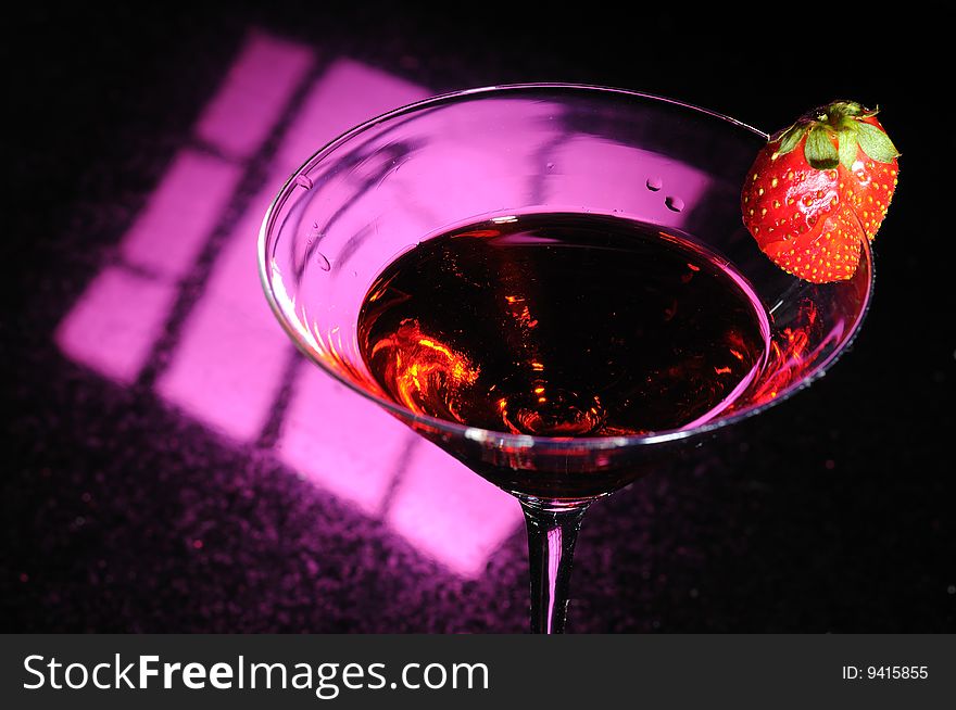 A martini glass with red liquid and a strawberry placed on the side. A martini glass with red liquid and a strawberry placed on the side