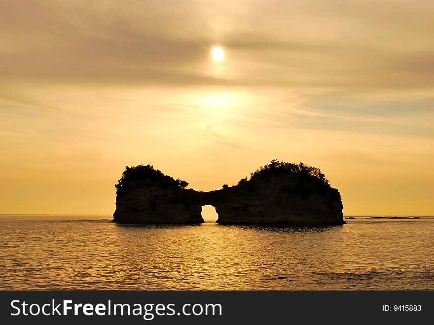 View of sun setting behind a uniquely shaped island with an opening at the bottom. View of sun setting behind a uniquely shaped island with an opening at the bottom
