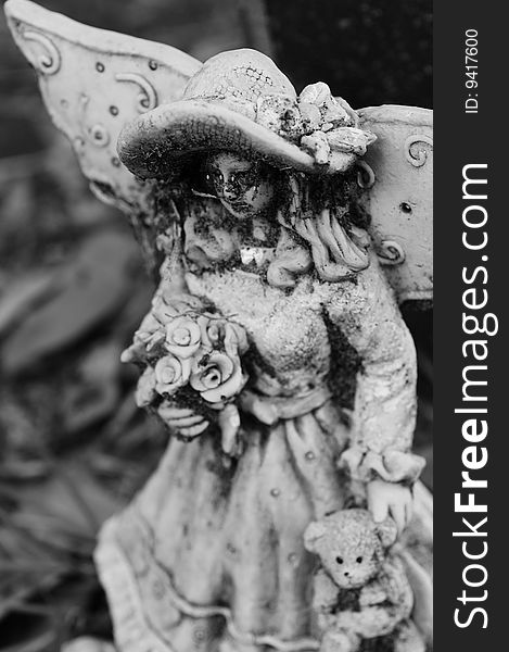 Creepy black and white statue of a young angel holding flowers and a teddy bear. Creepy black and white statue of a young angel holding flowers and a teddy bear