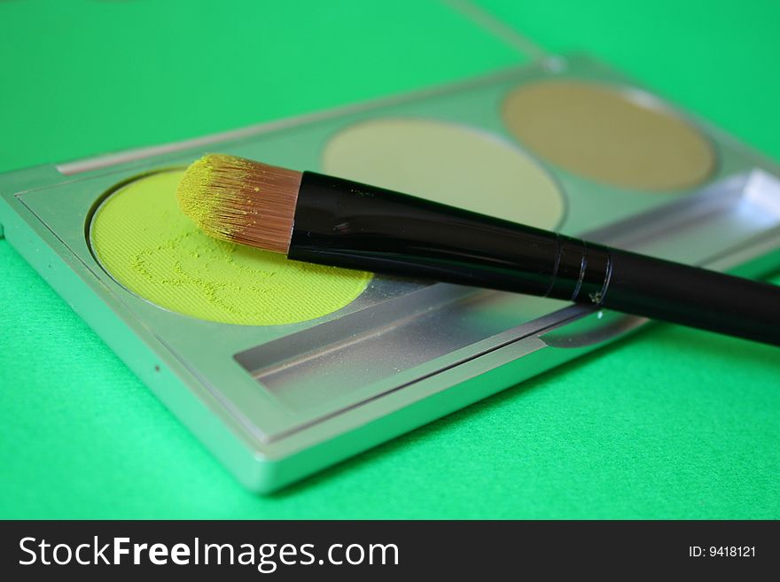 A set of three different green eyeshadow with brush and green background. A set of three different green eyeshadow with brush and green background